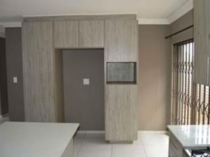 Modern kitchen featuring light wood-grain cabinetry, stone countertops, a built-in hob, and a secure sliding door with a metal security gate.