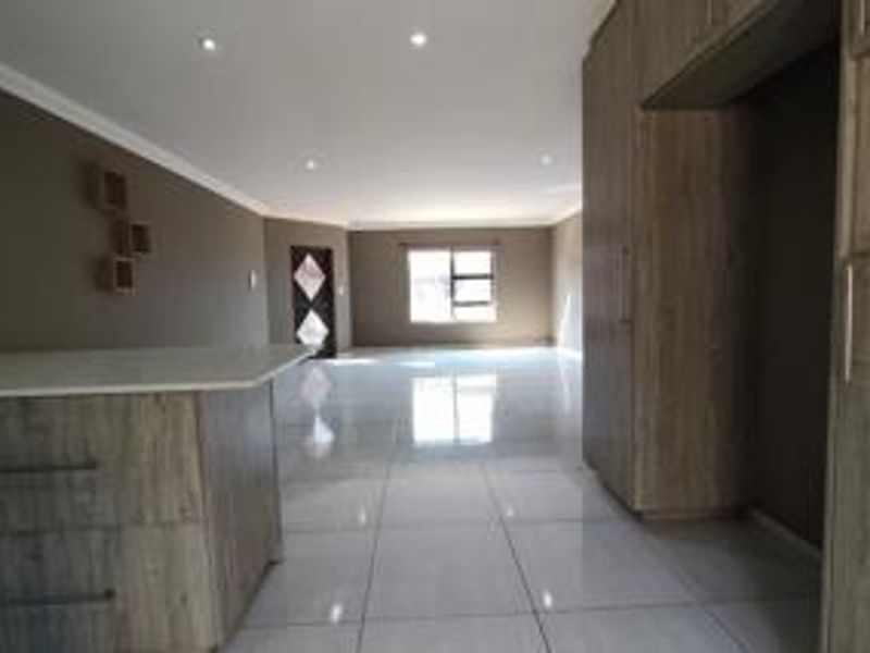 Spacious open-plan living area featuring modern tiled flooring, recessed downlighting, and built-in kitchen cabinetry with a central island.