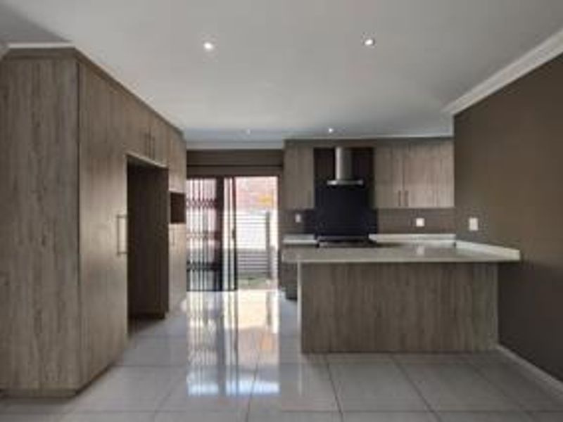Modern kitchen featuring light wood-grain cabinetry, stone countertops, integrated hob and extractor fan, with sleek tiled flooring and direct access to the exterior.