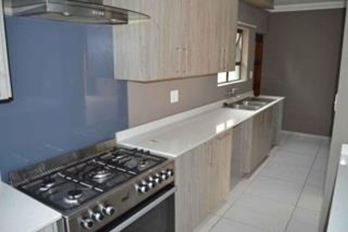 Modern kitchen featuring light wood-grain cabinetry, white quartz countertops, a gas stove with extractor fan, and a double basin sink.