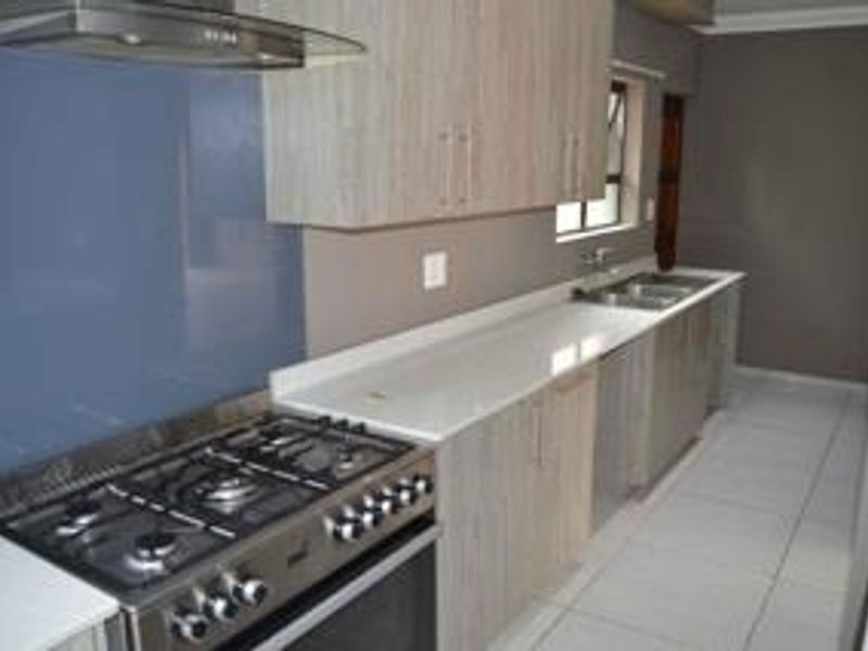 Modern kitchen featuring light wood-grain cabinetry, white quartz countertops, a gas stove with extractor fan, and a double basin sink.