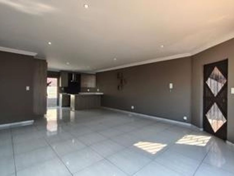 Spacious open-plan living area featuring polished porcelain floor tiles, recessed lighting, and a modern kitchen with built-in cabinetry and an island.
