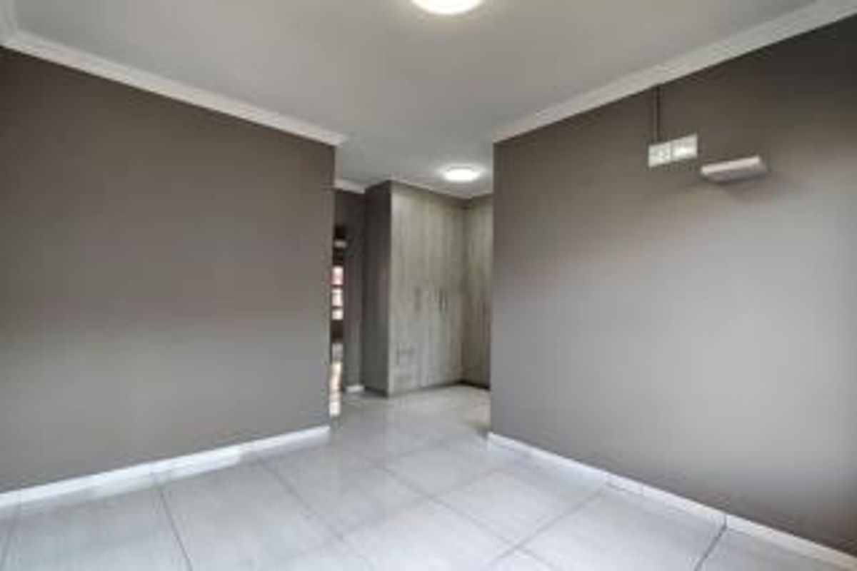 A clean, empty bedroom featuring neutral grey walls, tiled flooring, and built-in cupboards with modern wood-grain finish.