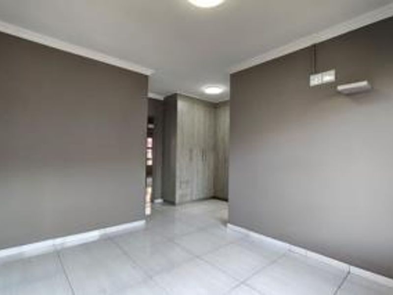 A clean, empty bedroom featuring neutral grey walls, tiled flooring, and built-in cupboards with modern wood-grain finish.
