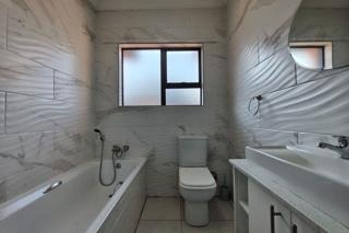 A modern, clean bathroom featuring white marble-look textured wall tiles, a bathtub with a handheld shower, a toilet, and a vanity with a basin.