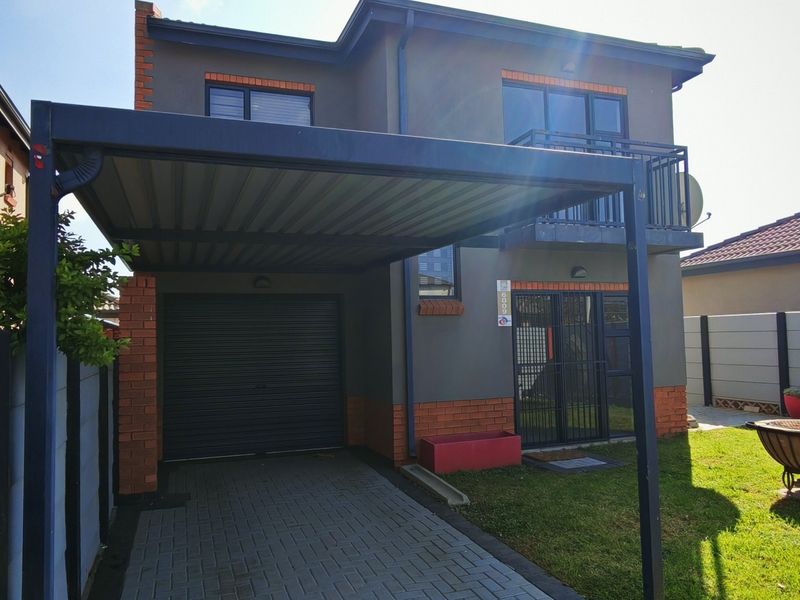 Front view of a two-story house featuring a paved driveway, a covered carport, a garage, and a small balcony.