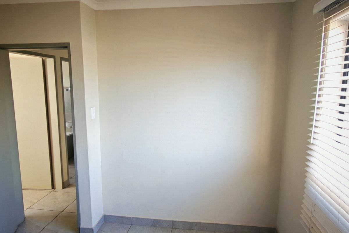 An empty bedroom featuring neutral wall tones, tiled flooring, and fitted venetian blinds, offering a clean and versatile space.
