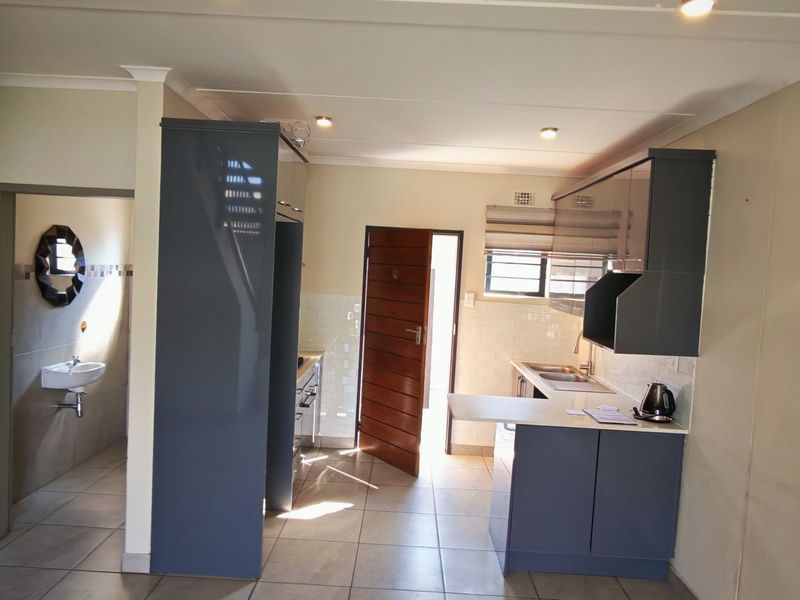 A modern, open-plan kitchen featuring sleek grey cabinetry, tiled flooring, and a functional layout with direct access to an adjacent bathroom area.