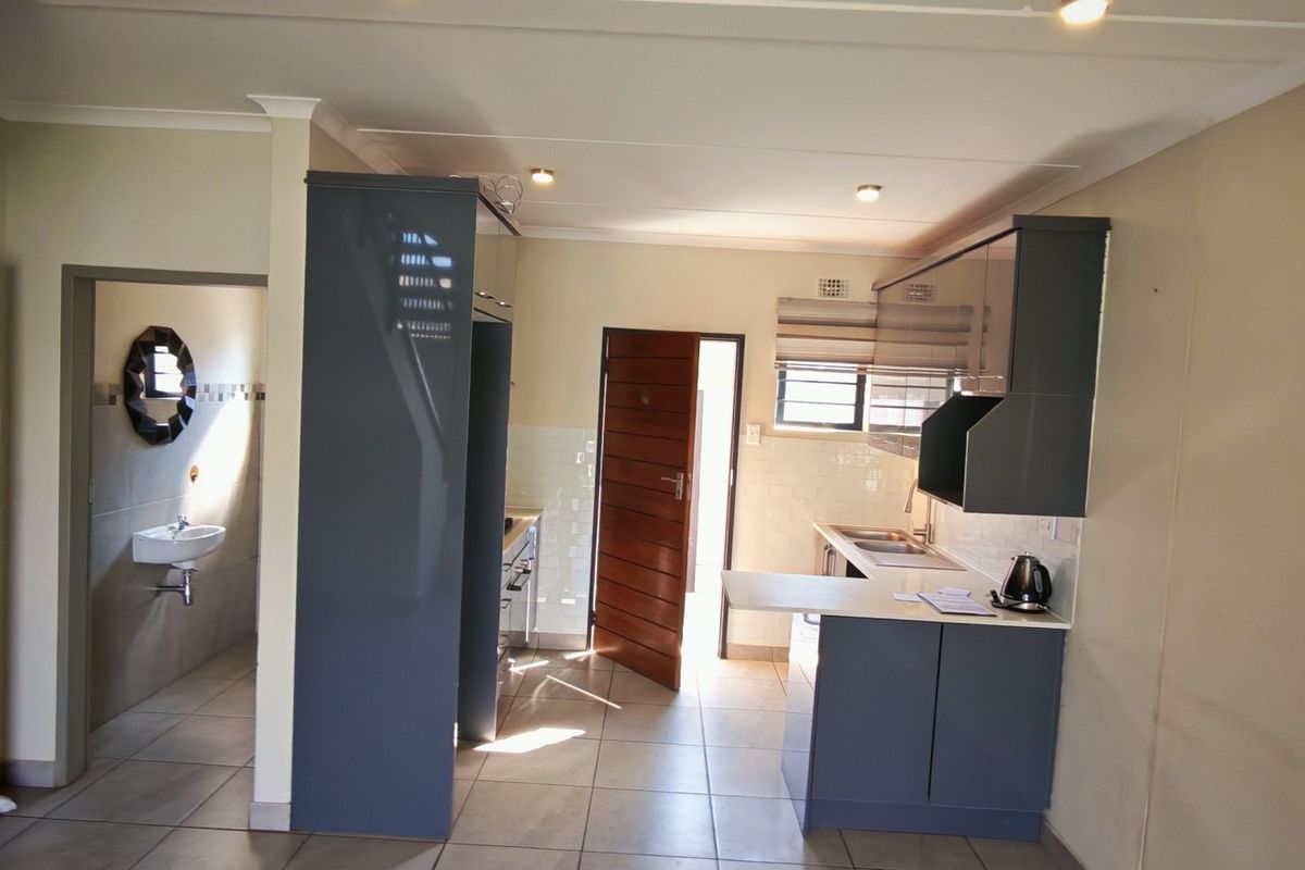 A modern, open-plan kitchen featuring sleek grey cabinetry, tiled flooring, and a functional layout with direct access to an adjacent bathroom area.
