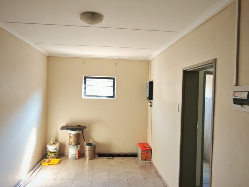 A clean, empty utility space featuring tiled flooring, a louver window, and wall-mounted electrical and security infrastructure.