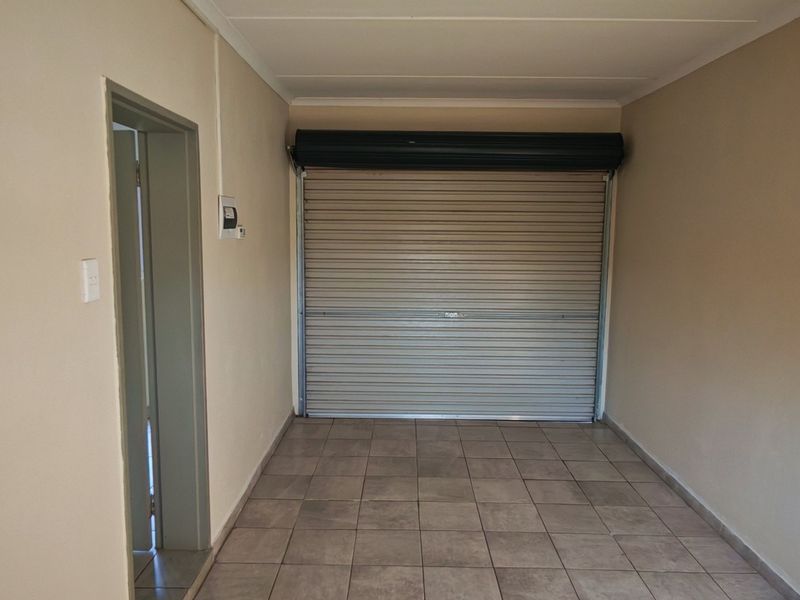 A clean, empty garage space featuring tiled flooring and a secure roller shutter door with convenient internal access.