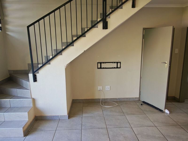 An open hallway area featuring tiled flooring, a staircase with a metal balustrade, and wall-mounted electrical and TV connectivity points.