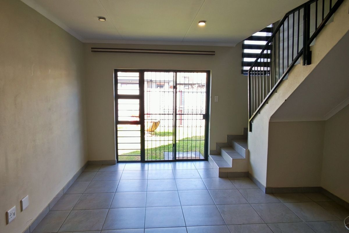 An open-plan living area featuring tiled flooring, a staircase with a metal balustrade, and a sliding glass door providing access to the rear garden.
