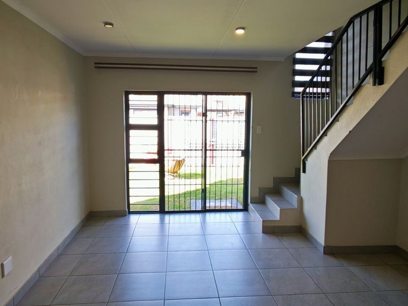 An open-plan living area featuring tiled flooring, a staircase with a metal balustrade, and a sliding glass door providing access to the rear garden.