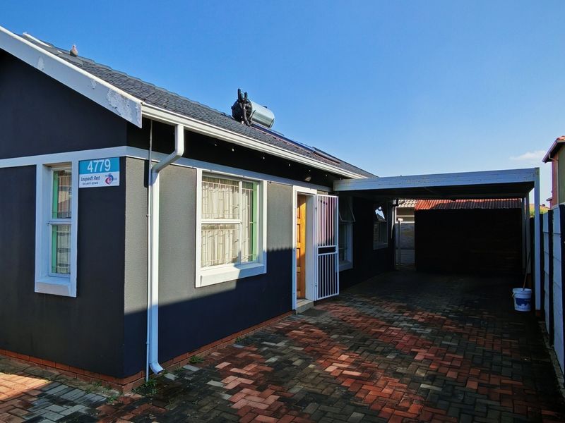 Front exterior view of a residential house featuring a paved driveway, carport, and solar geyser installation.