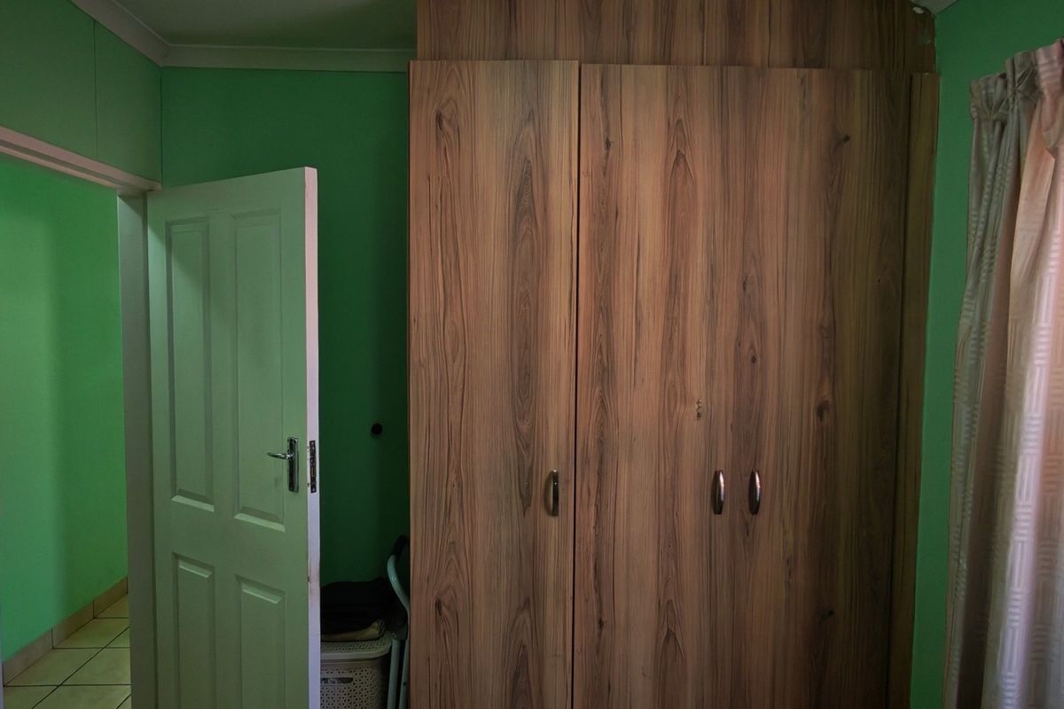 A bedroom featuring built-in wooden cupboards and a window with security bars, finished with green painted walls.