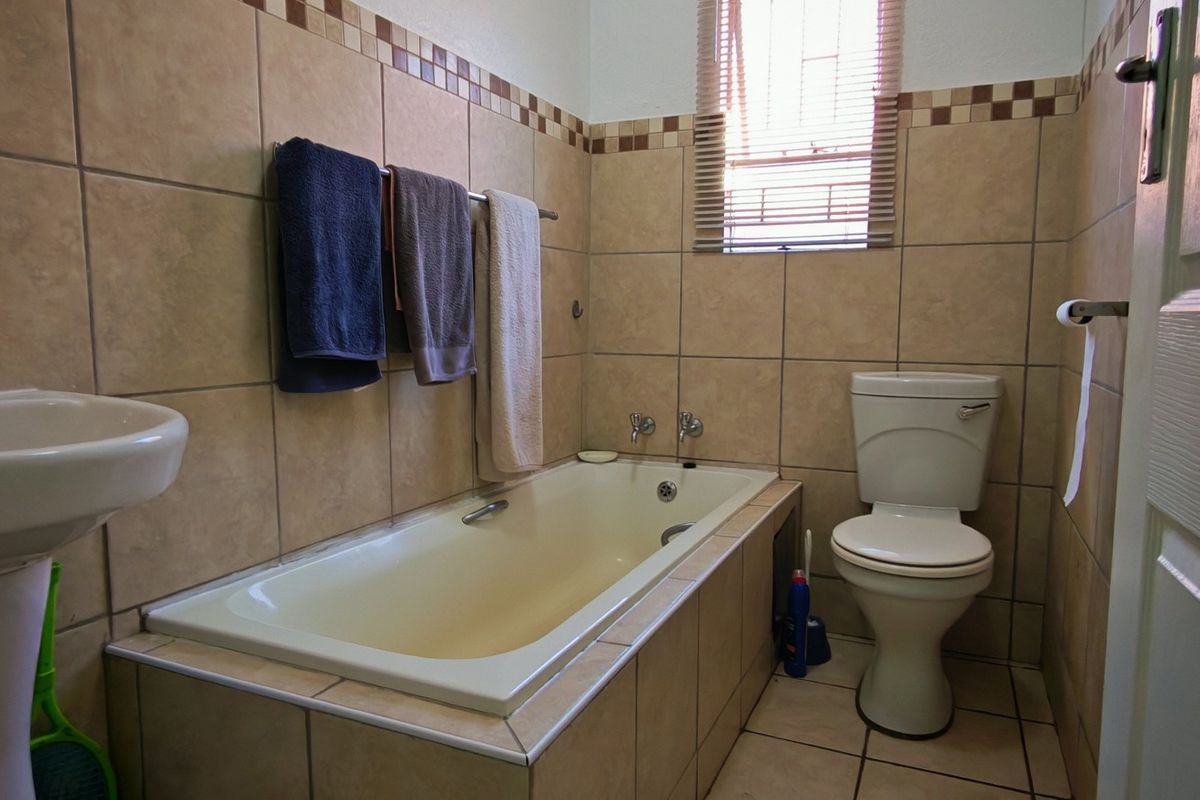 A functional bathroom featuring a built-in bathtub, pedestal basin, and toilet, finished with neutral ceramic wall and floor tiles.