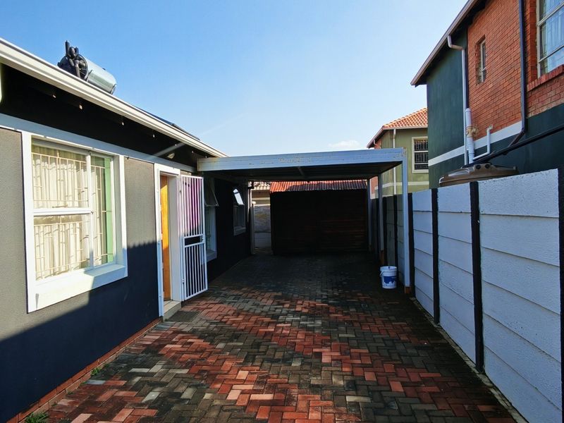 A paved driveway leading to a carport, featuring a secure boundary wall and exterior access to the property.