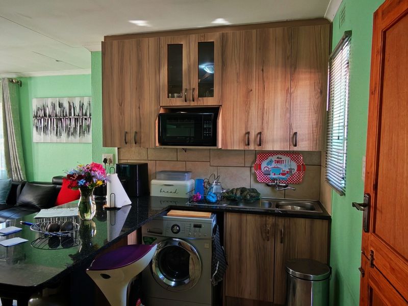 Open-plan kitchen area featuring wood-finish cabinetry, granite countertops, a double sink, and integrated appliances, seamlessly flowing into the adjacent living space.