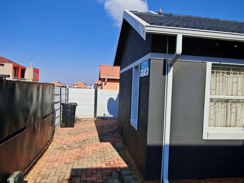 Exterior view of the property featuring a paved driveway, metal sliding gate, precast boundary wall, and a tiled roof with a solar water heater.