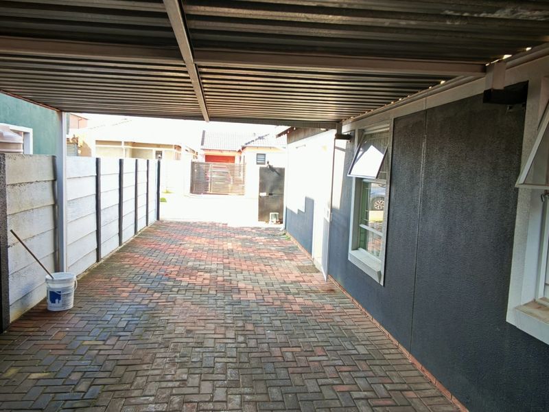 A covered carport area featuring paved flooring, a corrugated metal roof, and secure perimeter walling with window access to the main dwelling.