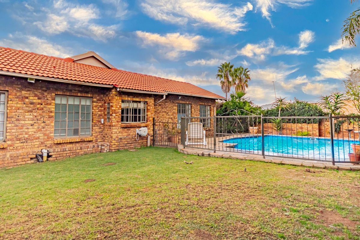 Rear exterior view of the house featuring a brick facade, tiled roof, and a fenced swimming pool set within a private garden area.