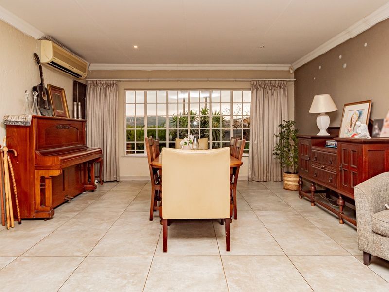 Spacious dining room featuring large grid-pattern windows, tiled flooring, and a wall-mounted air conditioning unit, offering a bright and functional space for family meals.