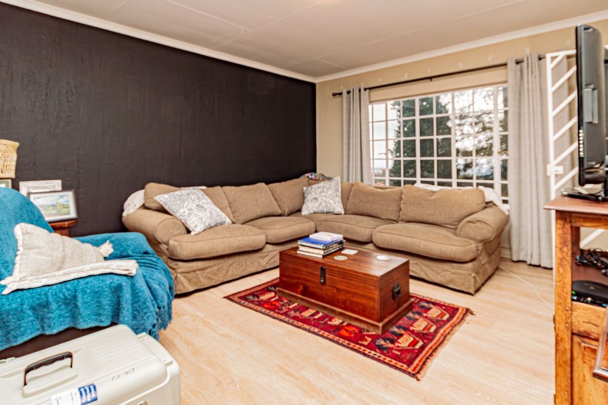A comfortable living room featuring light-toned laminate flooring, a large grid-pattern window, and a dark accent wall.