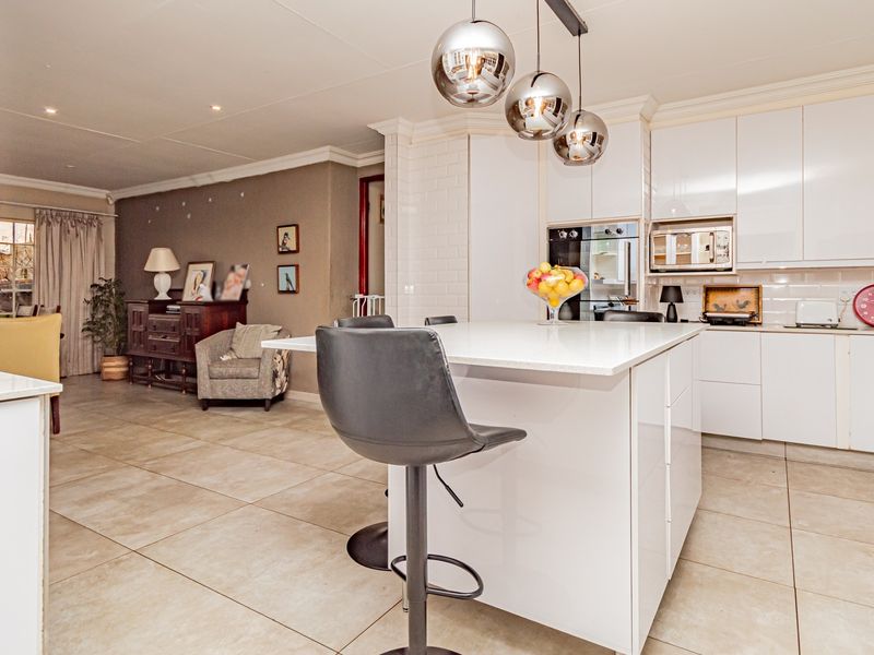 Modern open-plan kitchen featuring a central island, sleek white cabinetry, built-in appliances, and contemporary pendant lighting, seamlessly flowing into the adjacent living area.