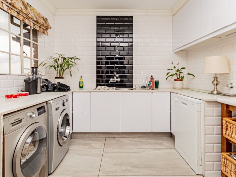 A functional laundry room featuring white cabinetry, subway tile backsplash, integrated sink, and space for multiple appliances with tiled flooring.