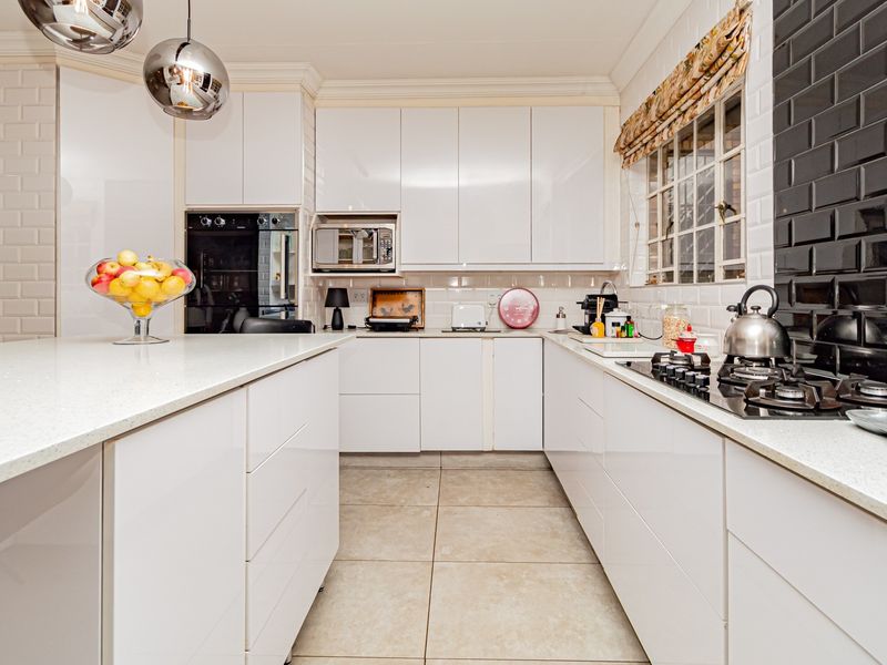 Modern kitchen featuring white gloss cabinetry, quartz countertops, a gas hob, built-in oven, and stylish subway tile backsplash.