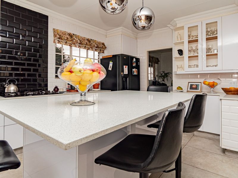 Modern kitchen featuring a large central island with quartz countertops, white cabinetry, black subway tile backsplash, and integrated lighting fixtures.