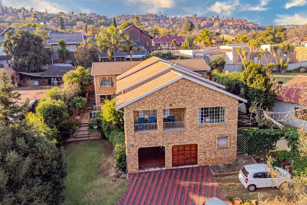 Aerial view of a double-story face brick house featuring a tiled roof, balcony, double garage, and a paved driveway set within a landscaped garden.