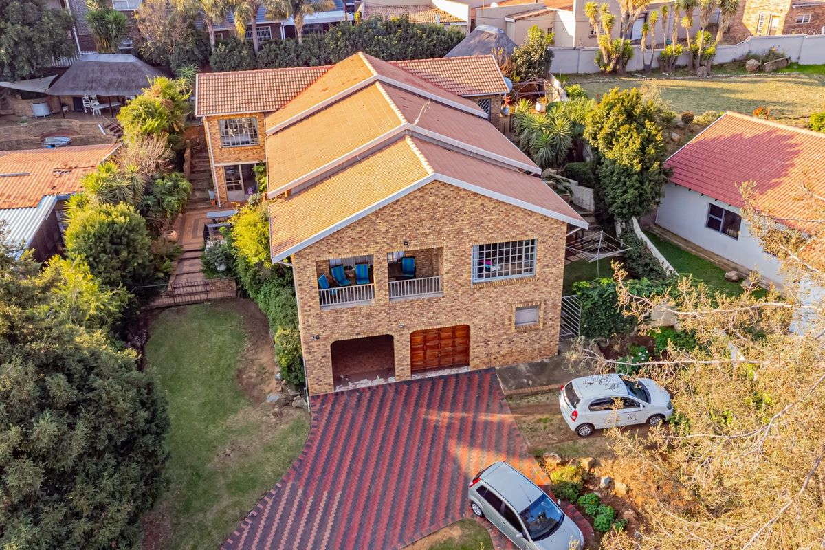 Aerial view of a double-story facebrick house featuring a tiled roof, paved driveway, integrated garage, and established garden surroundings.