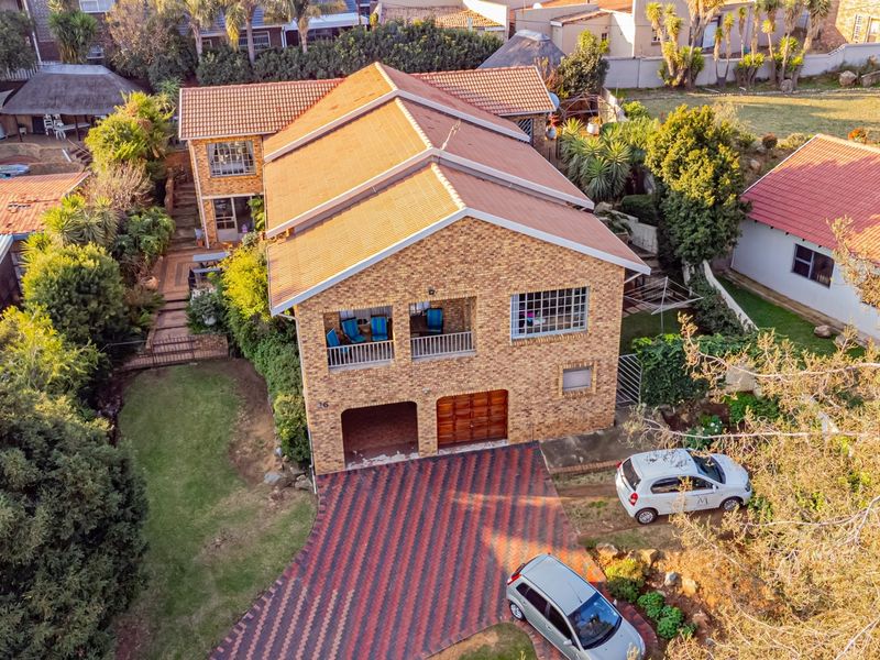 Aerial view of a double-story facebrick house featuring a tiled roof, paved driveway, integrated garage, and established garden surroundings.