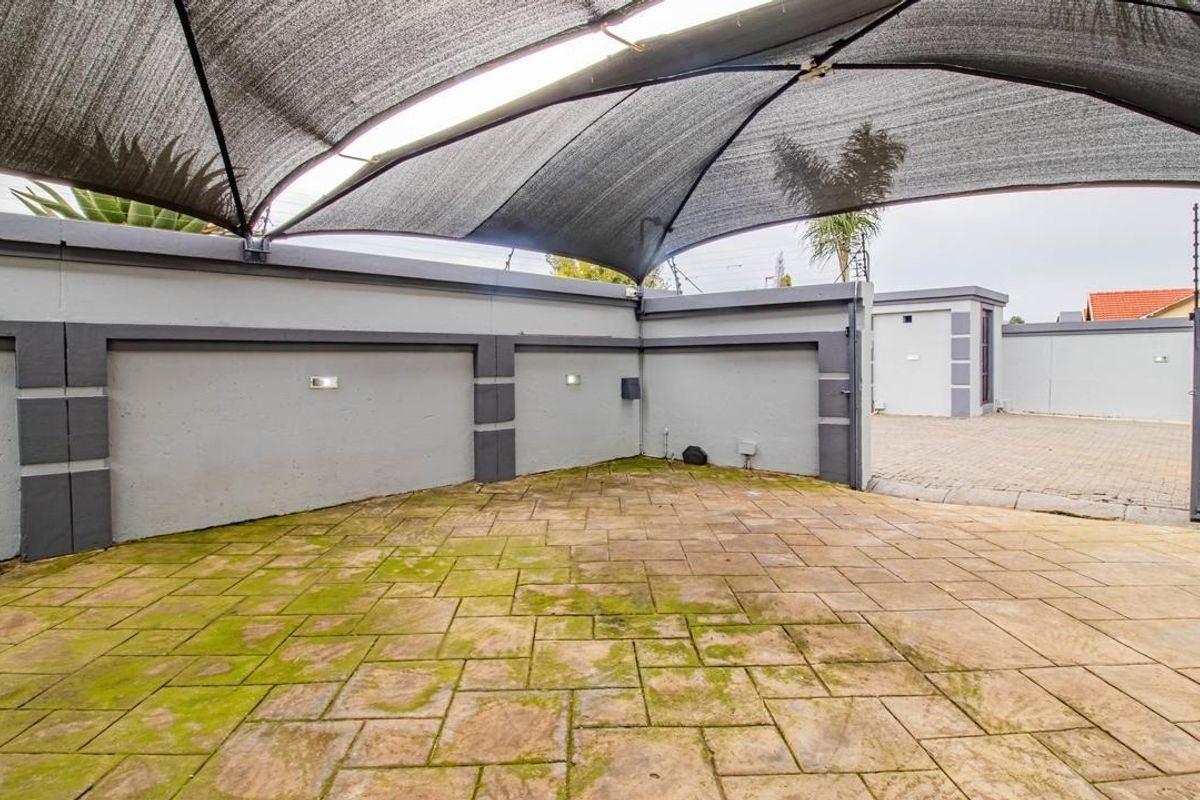 A paved outdoor area featuring a large shade sail, perimeter wall with integrated lighting, and electric fencing, providing a secure and shaded space.