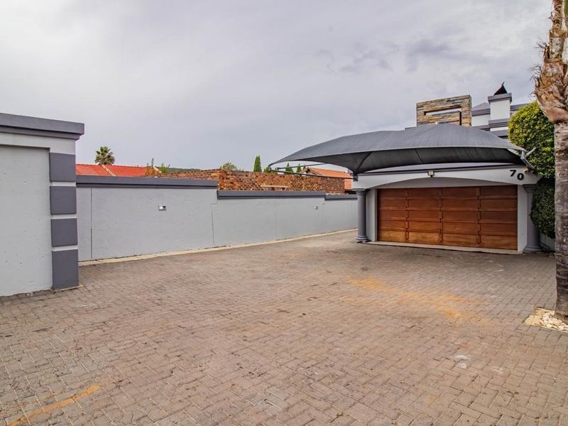 Front exterior view featuring a paved driveway, secure boundary walls, and a covered garage area with a wooden door.