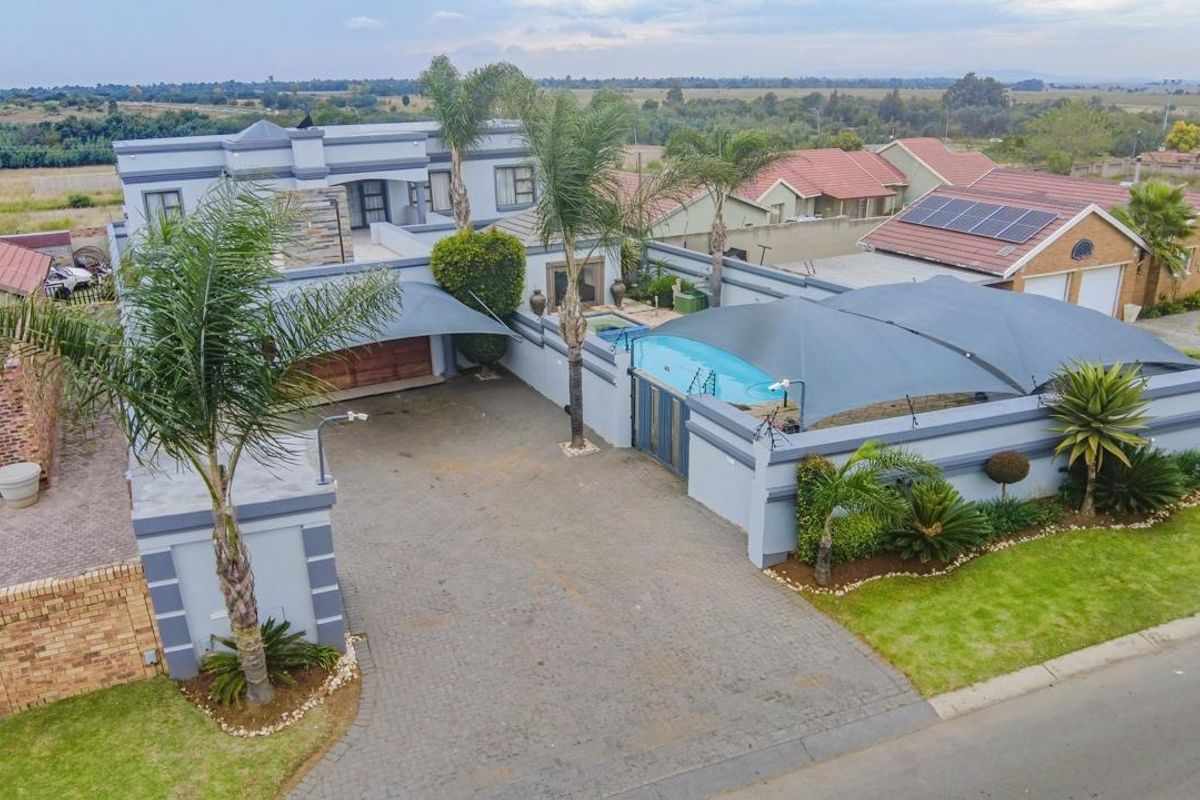 Aerial view of a residential property featuring a paved driveway, swimming pool with shade sails, and well-maintained boundary walls and landscaping.