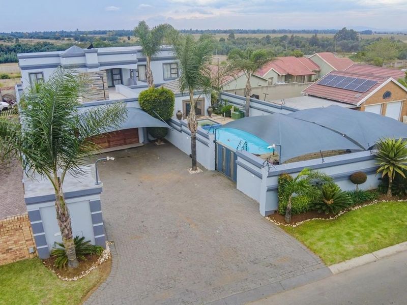 Aerial view of a residential property featuring a paved driveway, swimming pool with shade sails, and well-maintained boundary walls and landscaping.