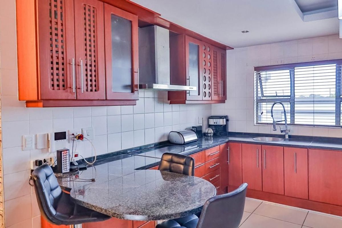 A functional kitchen featuring warm-toned wooden cabinetry, granite countertops, a breakfast nook, and a tiled backsplash with integrated stainless steel extractor fan.
