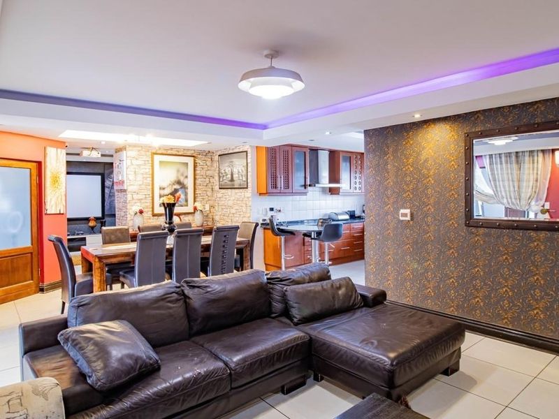 Spacious open-plan living and dining area featuring tiled floors, modern recessed lighting, a stone-clad feature wall, and an integrated kitchen with breakfast bar.