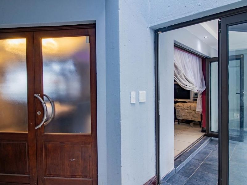 Entrance area featuring a double wooden door with frosted glass panels and an adjacent aluminium-framed glass door leading to an interior living space.