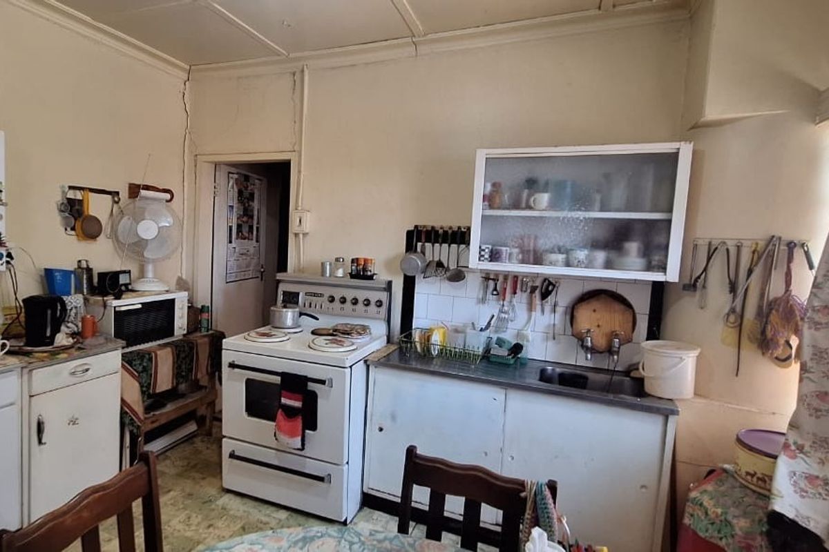 A dated kitchen featuring original cabinetry, a freestanding stove, and a stainless steel sink, requiring modernization to improve functionality and aesthetic appeal.