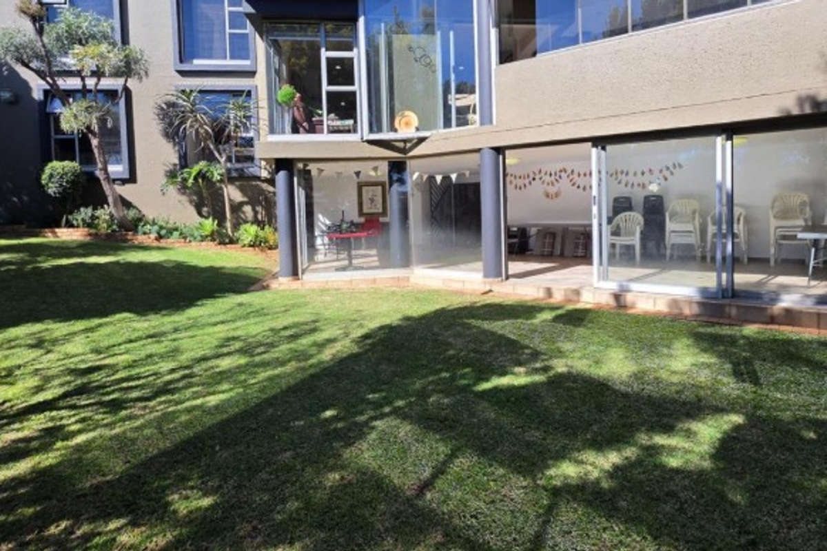 A view of the rear exterior of the house featuring a well-maintained lawn, large glass windows, and sliding doors leading to the interior.
