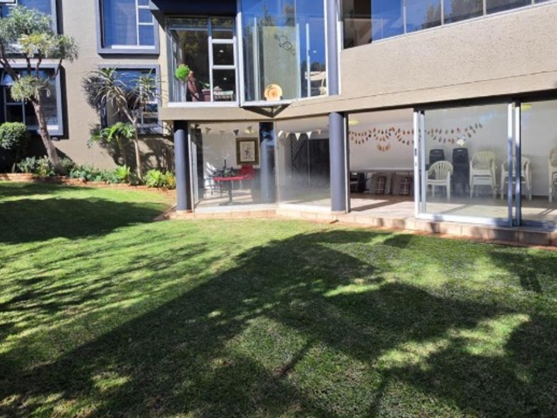 A view of the rear exterior of the house featuring a well-maintained lawn, large glass windows, and sliding doors leading to the interior.