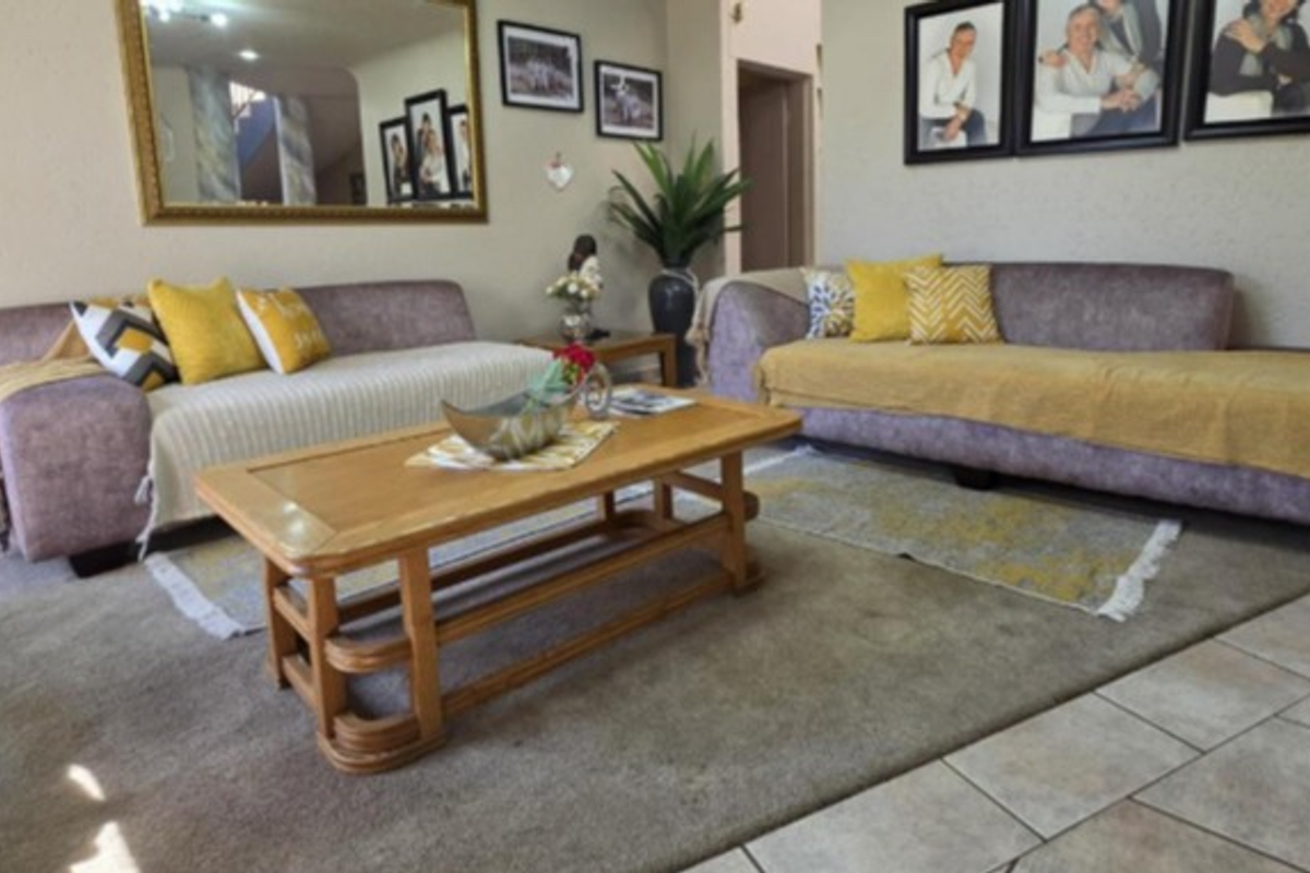 A comfortable living room featuring a mix of tiled and carpeted flooring, complemented by a large wall-mounted mirror.