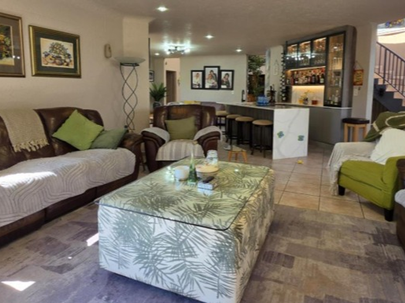 Spacious open-plan living area featuring a built-in bar, tiled flooring, recessed lighting, and an elegant staircase with a metal railing.