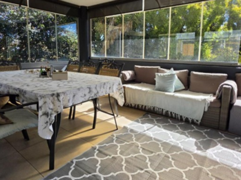 A covered patio area featuring tiled flooring and a glass sliding enclosure, providing a versatile outdoor living space.