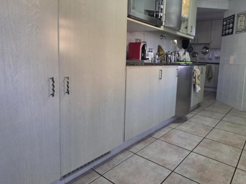 A functional kitchen featuring light-toned built-in cabinetry, tiled flooring, and integrated appliances, offering a practical layout with an adjacent pantry area.