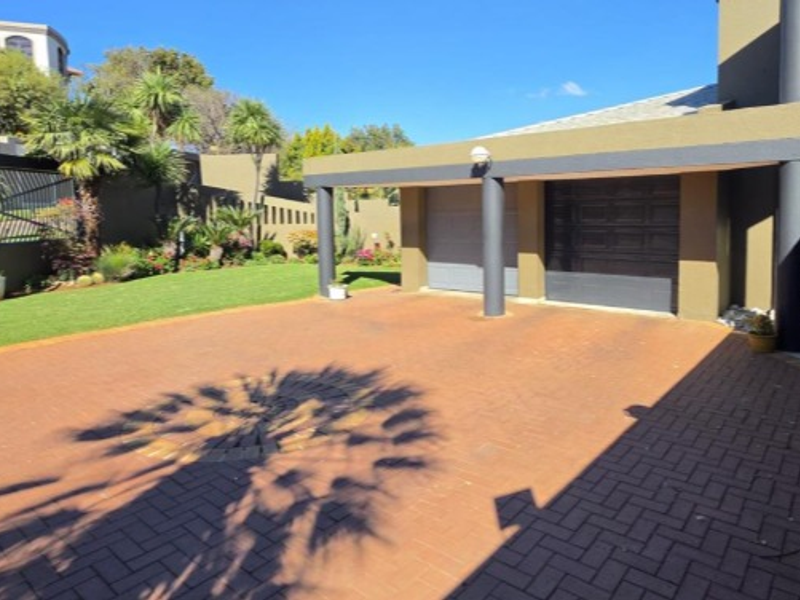 A well-maintained front exterior featuring a paved driveway, double garage, and landscaped garden area with established boundary walls.